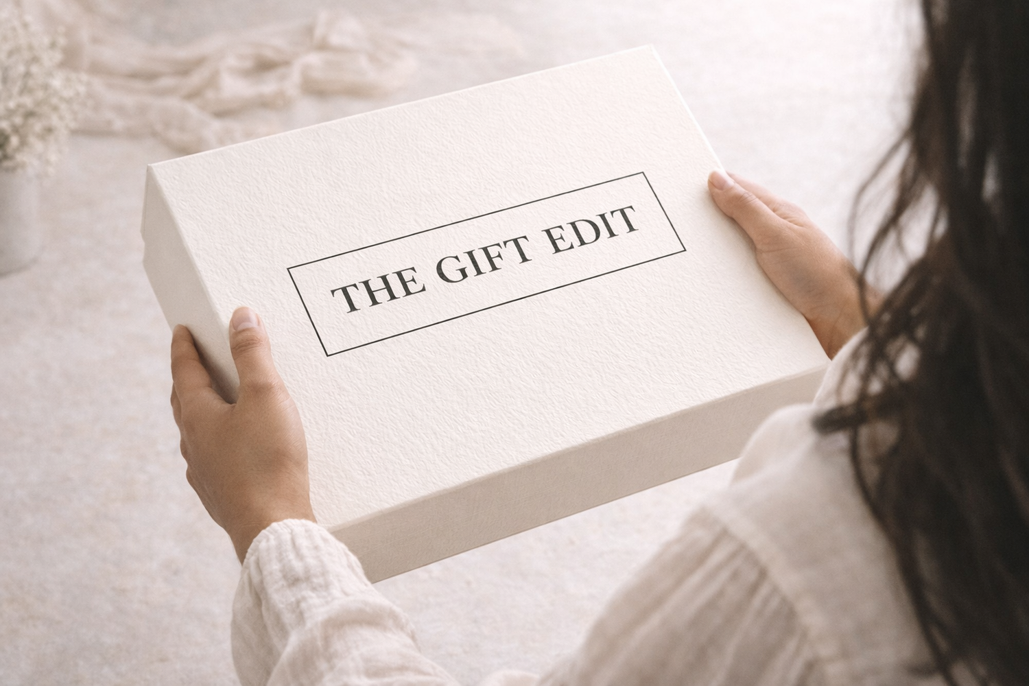 Person holding a box labeled 'THE GIFT EDIT' on a soft, light background